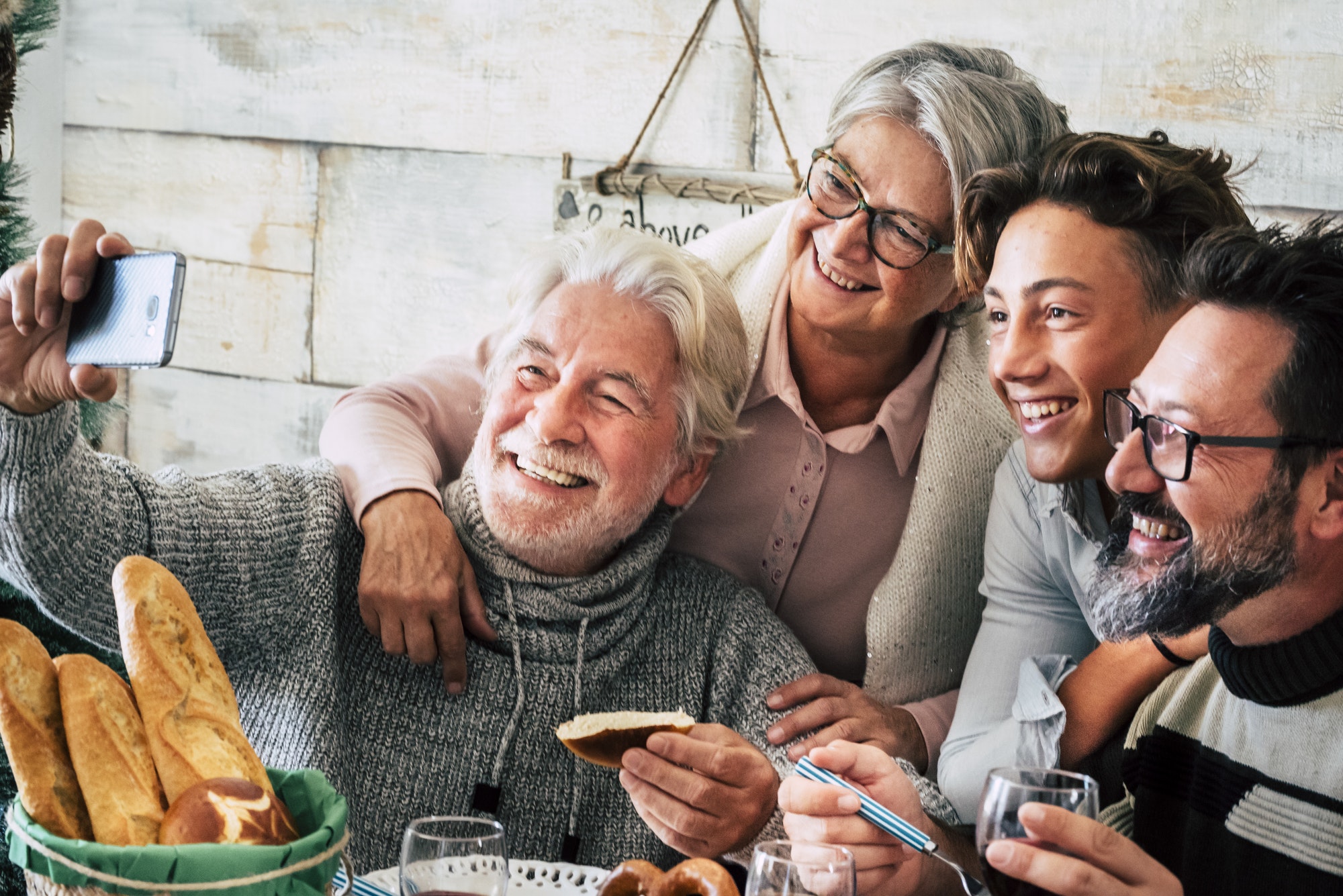 Senior man taking selfie using mobile phone with family on dining table at christmas